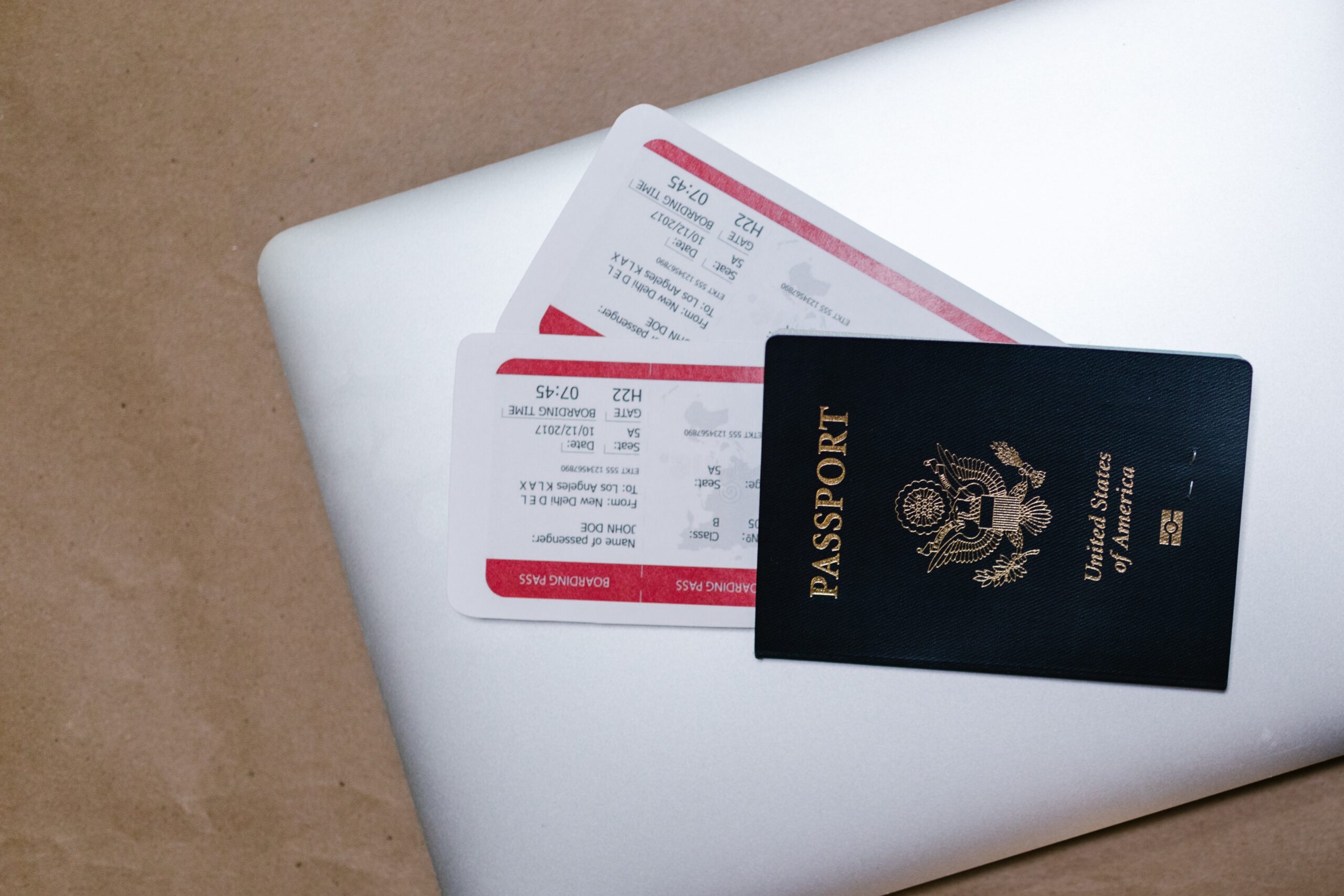 Czerwony paszport, z którego wystają dwa bilety lotnicze, leżący na białym zamkniętym laptopie