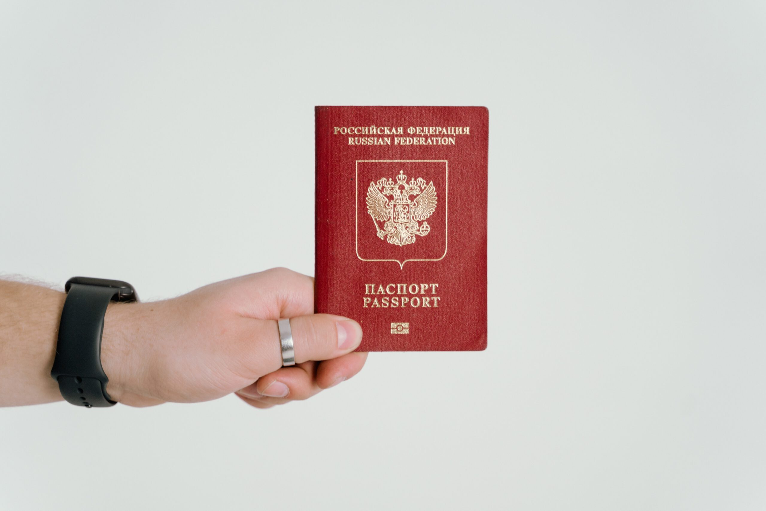 Dłoń z czarną opaską na ręce, trzymająca czerwony paszport na tle białej ściany