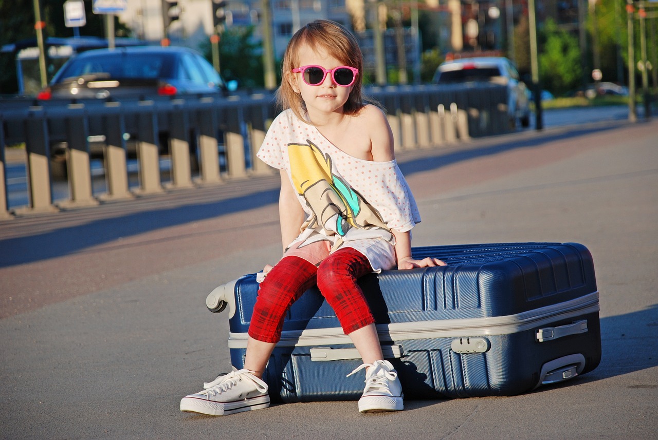 Mała dziewczynka w kolorowych ubraniach i okularach słonecznych, siedząca na walizce na stacji kolejowej Częstochowa Stradom