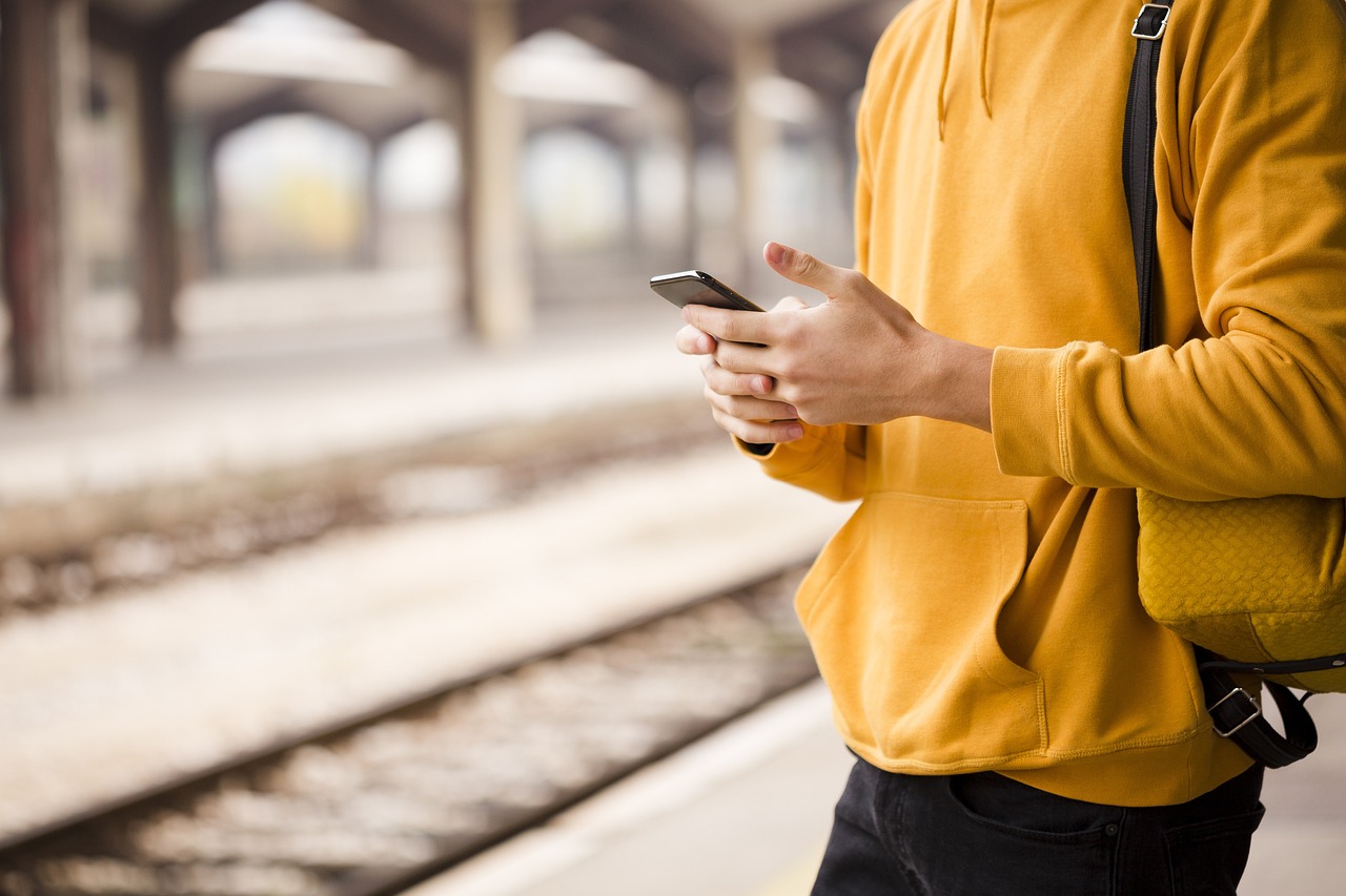 Młody mężczyzna w żółtej bluzie z telefonem w rękach na stacji kolejowej Częstochowa Stradom