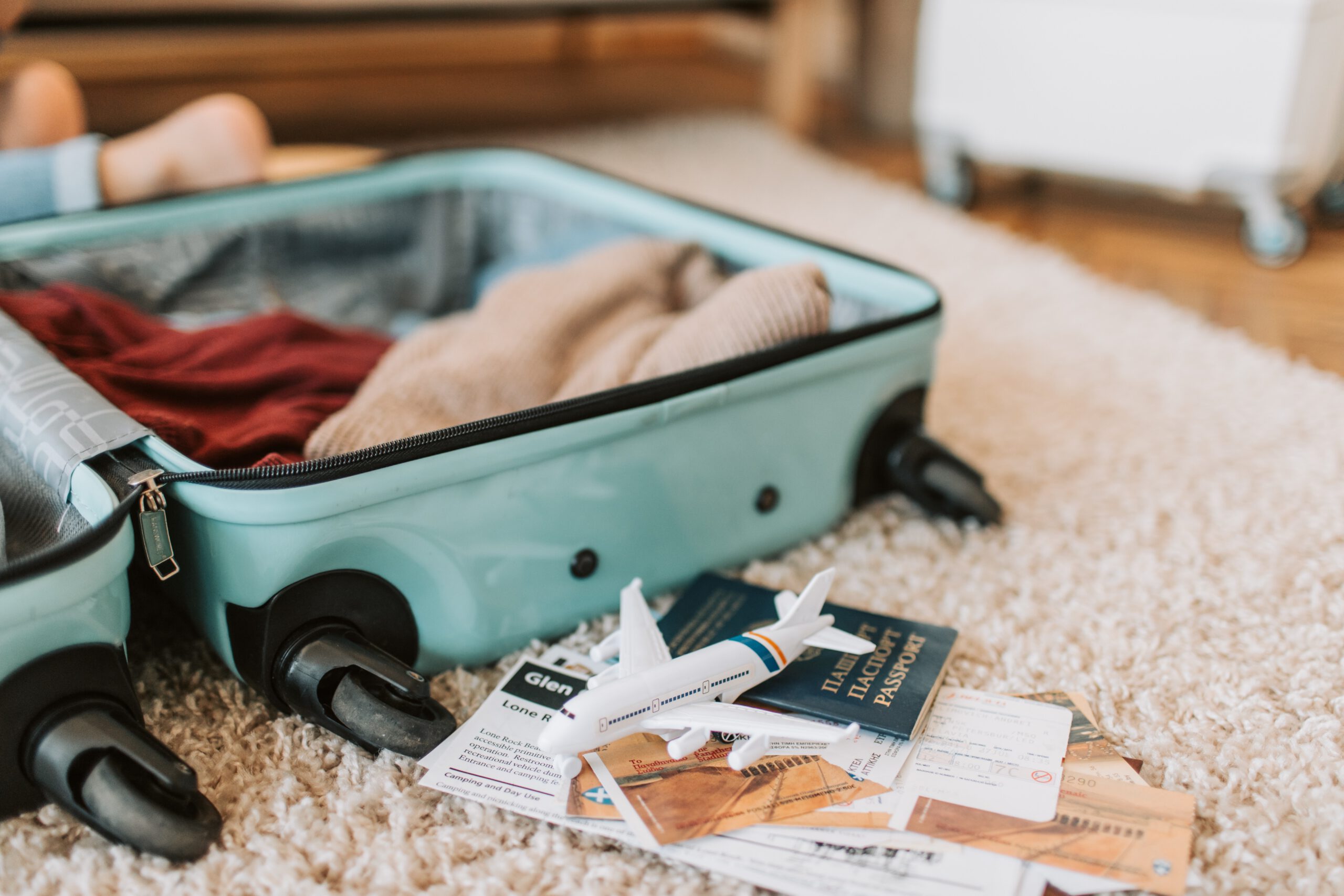 Paszport leżący na dywanie obok w połowie spakowanej walizki, przykryty w części ubraniami i innymi rzeczami