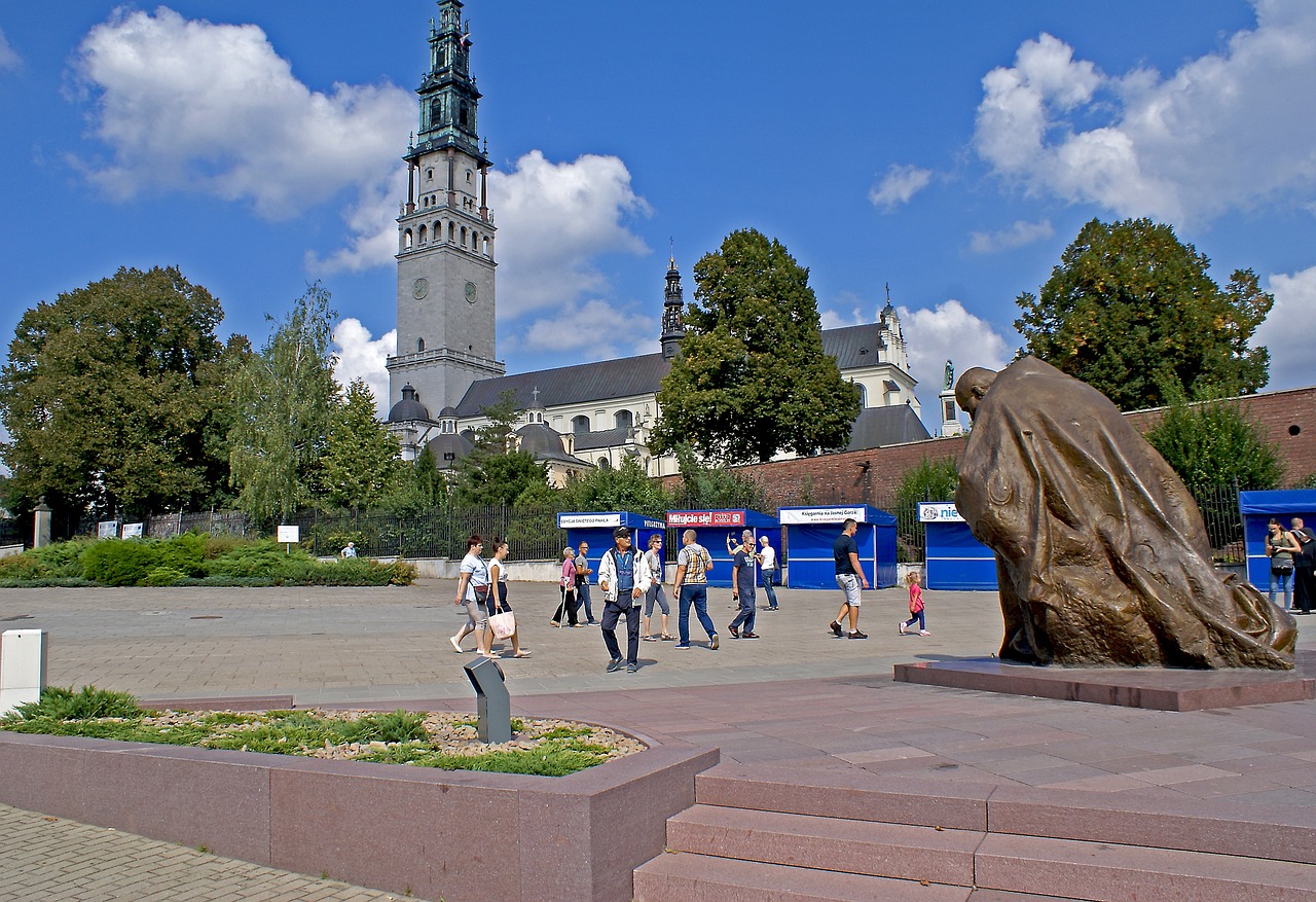 Plac przed sanktuarium na Jasnej Górze w Częstochowie z pomnikiem i spacerującymi ludźmi